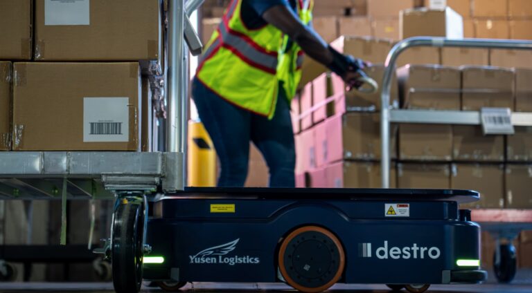 Warehouse employees and autonomous mobile robots coordinated by an AI workflow orchestration platform during transload operations.